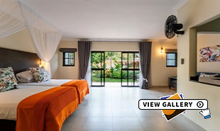 large hotel room with Twin beds pushed togther with red  and white covering. doors at back lead onto gardens