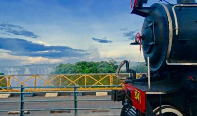Black and red front of a steam train with the Bridge and the spray from the Falls in the background