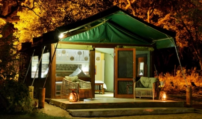 Interior of tent with bed and lighst on looking from outside with chairs on the deck