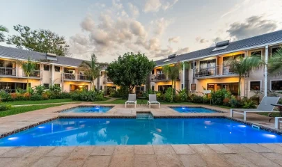 3 blue pools, one large, 2 smaller, with the rooms lit up in the background and gardens surrounding the pool