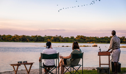 2 guests sitting in chairs riverside getting drinks served